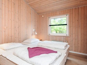 Habitación con paneles de madera, una cama, un ventanal y una lámpara fijada a la pared.