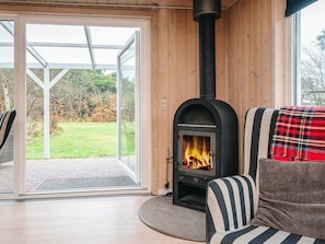 A modern interior with a wood-burning stove, a striped sofa, and a view of a green outdoor area through glass doors.