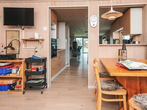 A kitchen with wooden cabinets, a dining table, and a television mounted on the wall.