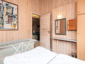 Una habitación con paneles de madera, una cama, una silla colgante, un cuadro, un espejo y una puerta que da a un baño.