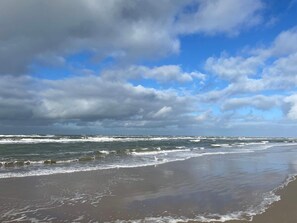Una playa con olas, cielo nublado y horizonte despejado.