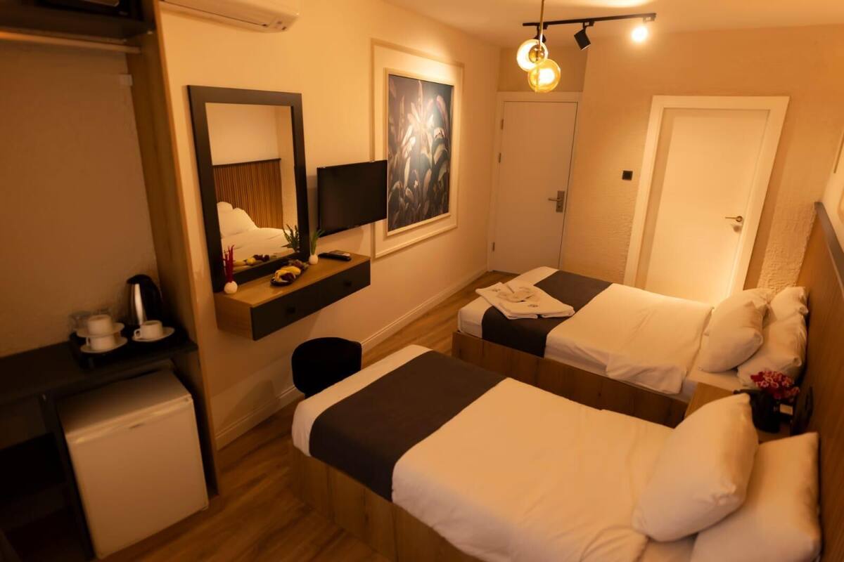 A hotel room with two beds, a desk with a coffee maker, a TV, and a painting on the wall.