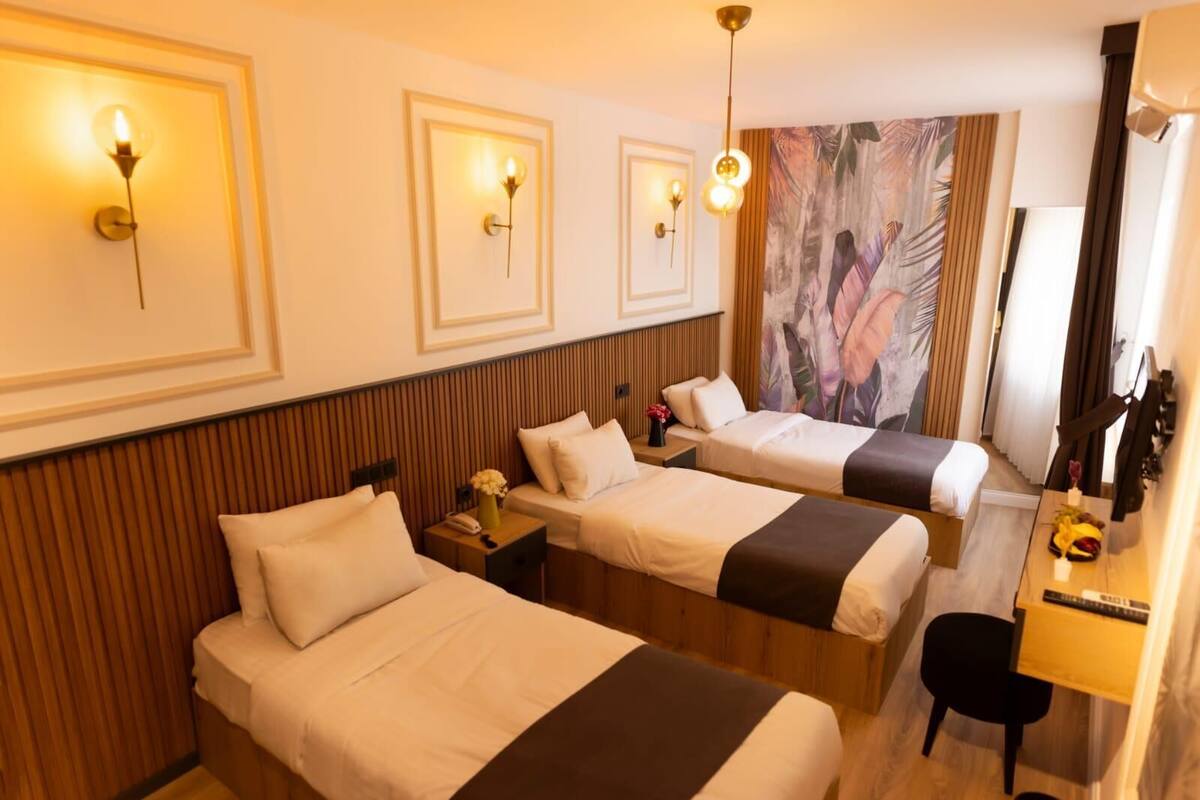A hotel room with three beds, wooden paneling, a large painting, and a desk with a chair.