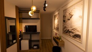 A hallway with a television, a small refrigerator, and a black chair. There are two hanging spherical lights and a painting on the wall. - Grand Isbilir Hotel (Nevşehir)