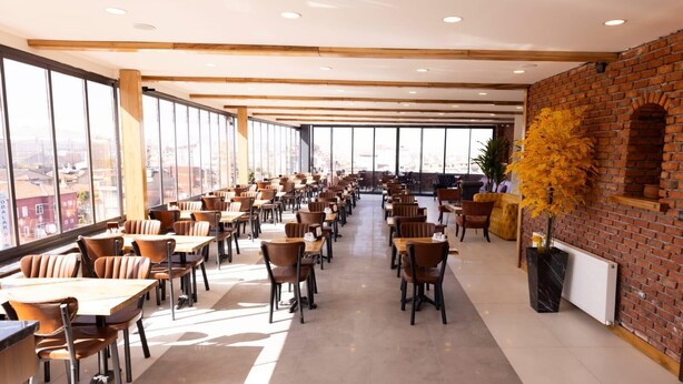 A spacious dining area with high ceilings, large windows, and a brick wall accent. Tables and chairs are arranged for dining. - Grand Isbilir Hotel (Nevşehir)