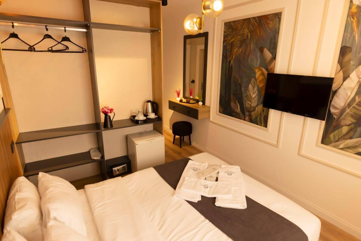 A hotel room with a bed, a desk with a chair, a mirror, a TV, and a painting.