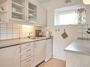 A kitchen with white cabinets, a coffee maker, and a window with curtains. - 2 Person Holiday Home in Aakirkeby (Akirkeby)
