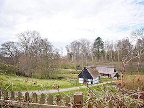 A traditional thatched-roof house with a white and black exterior, surrounded by a wooden fence and a grassy field. - 2 Person Holiday Home in Aakirkeby (Akirkeby)