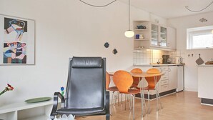 A modern kitchen with white cabinets, a dining table with orange chairs, and a black leather chair.
