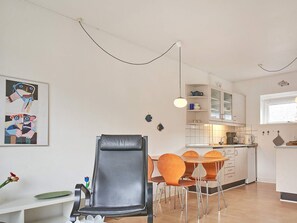 A modern kitchen with white cabinets, a dining table with orange chairs, and a black leather chair. - 2 Person Holiday Home in Aakirkeby (Akirkeby)