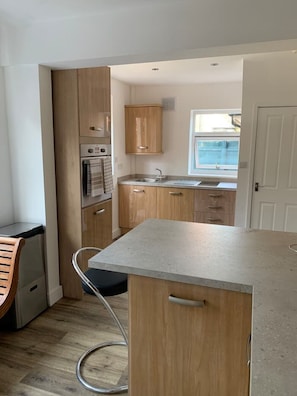 A compact kitchen with wooden cabinets, a built-in oven, and a window providing natural light. - Peaceful renovated home, fab location, pet friendly, garden & parking sleeps 5 (Chester)
