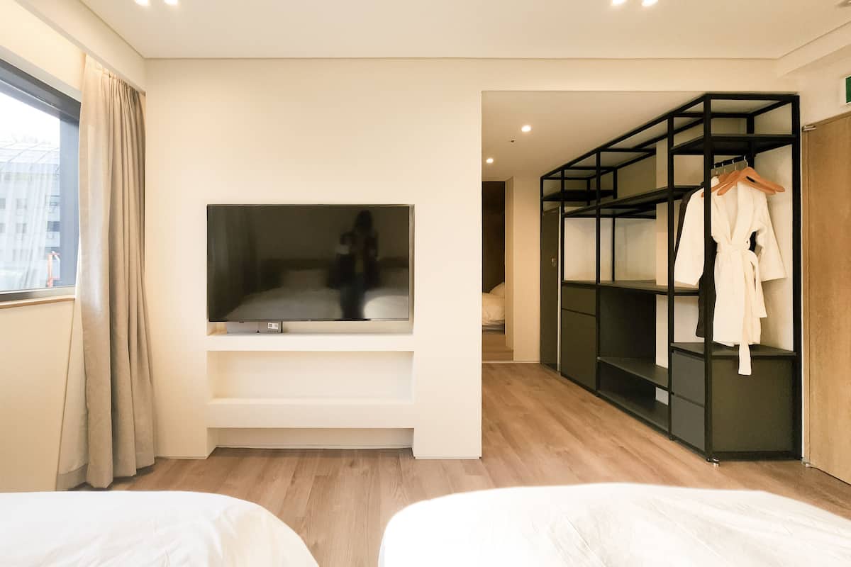 Une chambre d’hôtel moderne avec deux lits, une télévision, un dressing et une vue sur la ville.