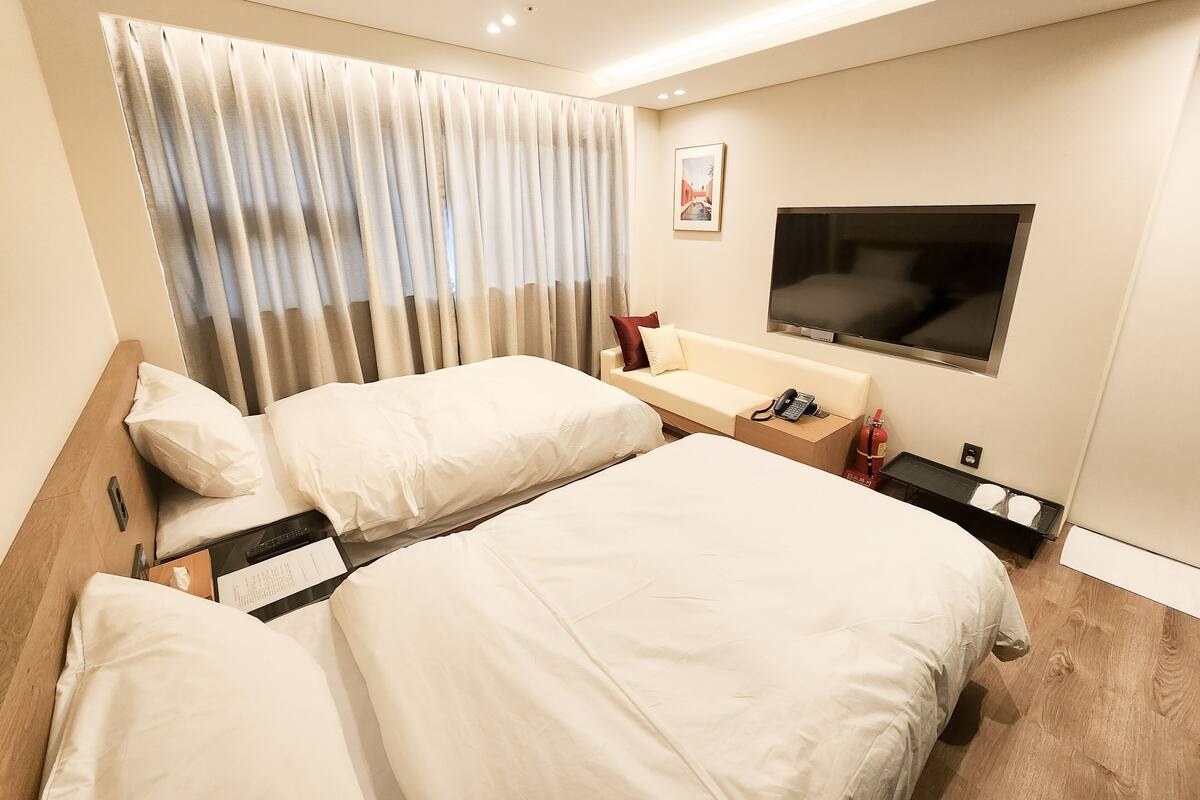 Une chambre d’hôtel avec deux lits, un canapé, une télévision et une fenêtre avec des rideaux.