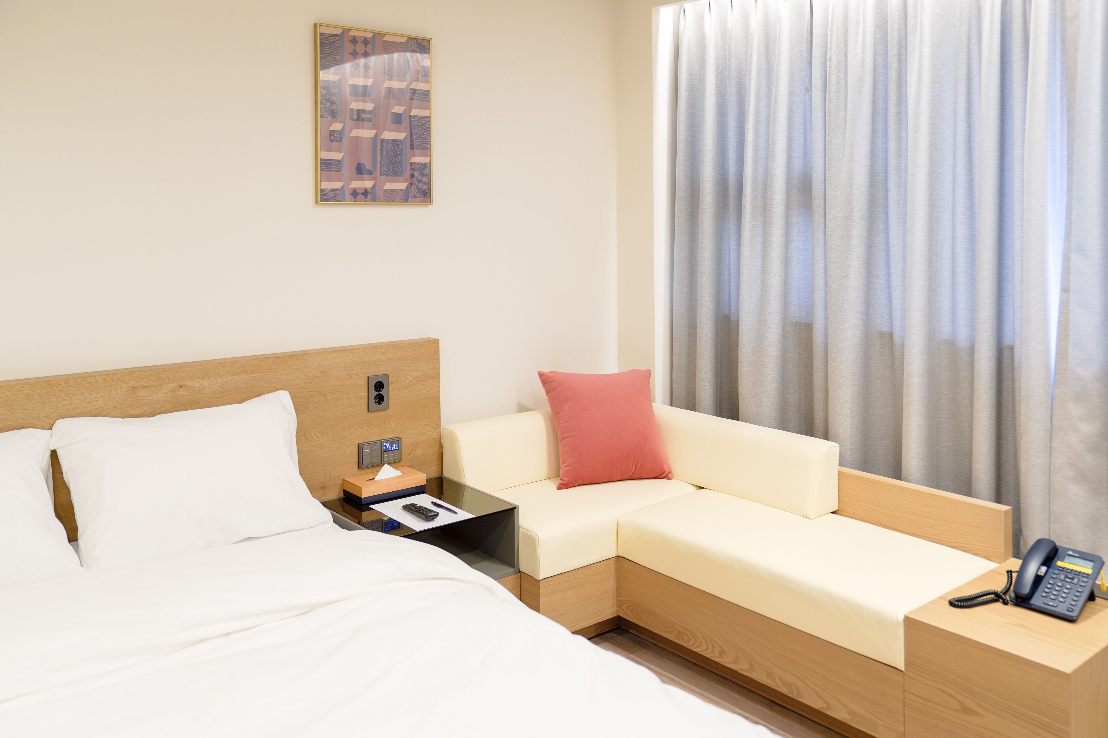 Una habitación de hotel con cama, sofá, mesita de noche con teléfono y ventana con cortinas.