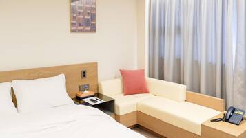 Una habitación de hotel con cama, sofá, mesita de noche con teléfono y ventana con cortinas.