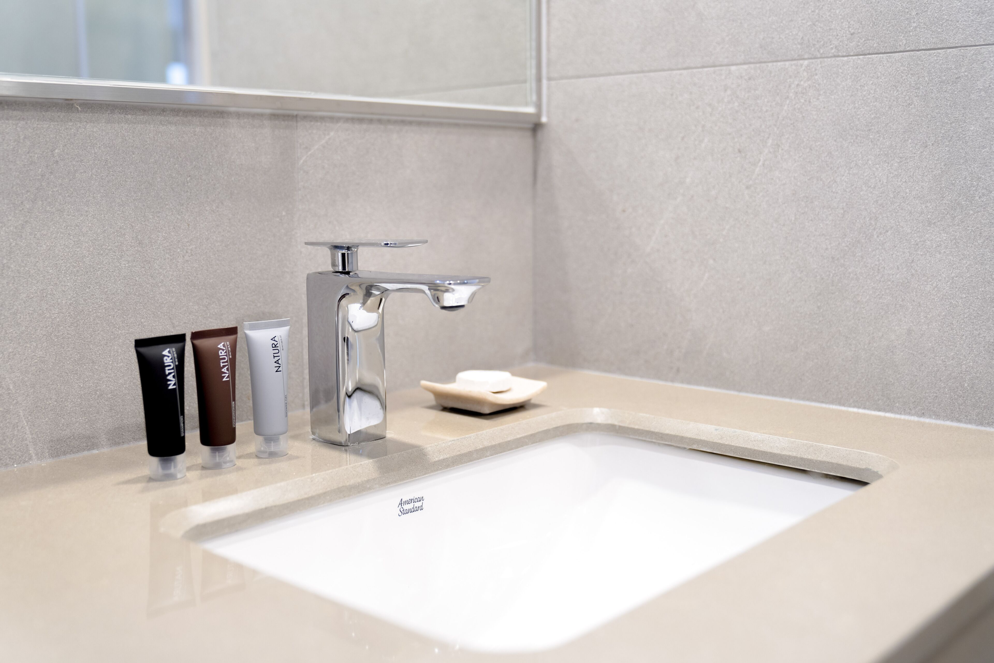 A bathroom with a white sink, a chrome faucet, and three tubes of NATURE soap.