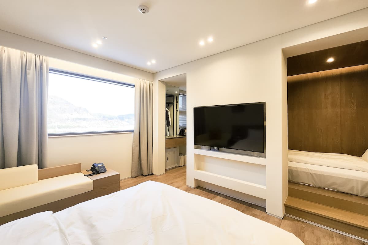 Une chambre d’hôtel moderne dotée d’un grand lit, d’un téléviseur fixé au mur, d’un coin salon avec un canapé et d’une fenêtre avec des rideaux.
