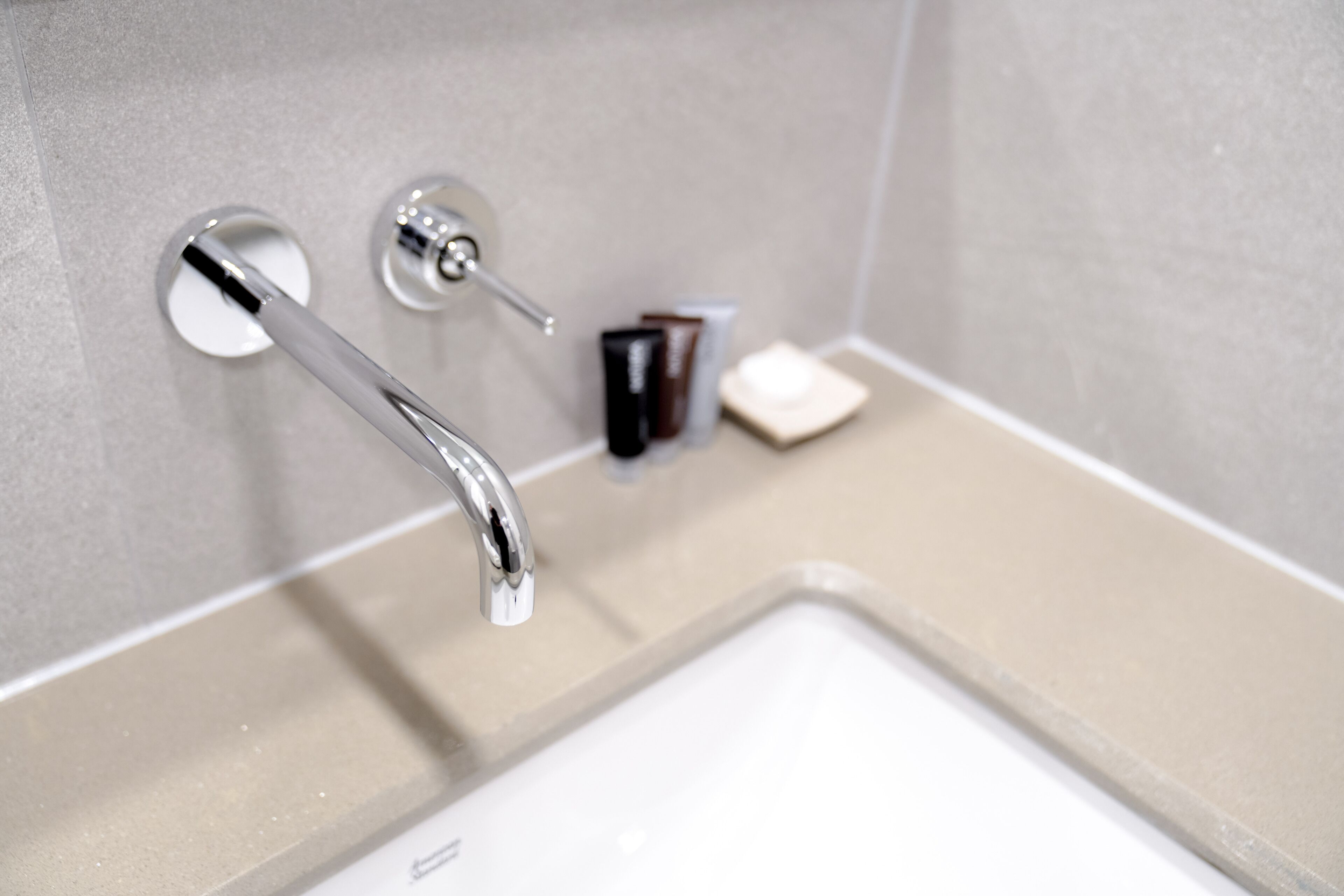 A modern bathroom with a chrome faucet, a soap dispenser, and a small bottle of shampoo.