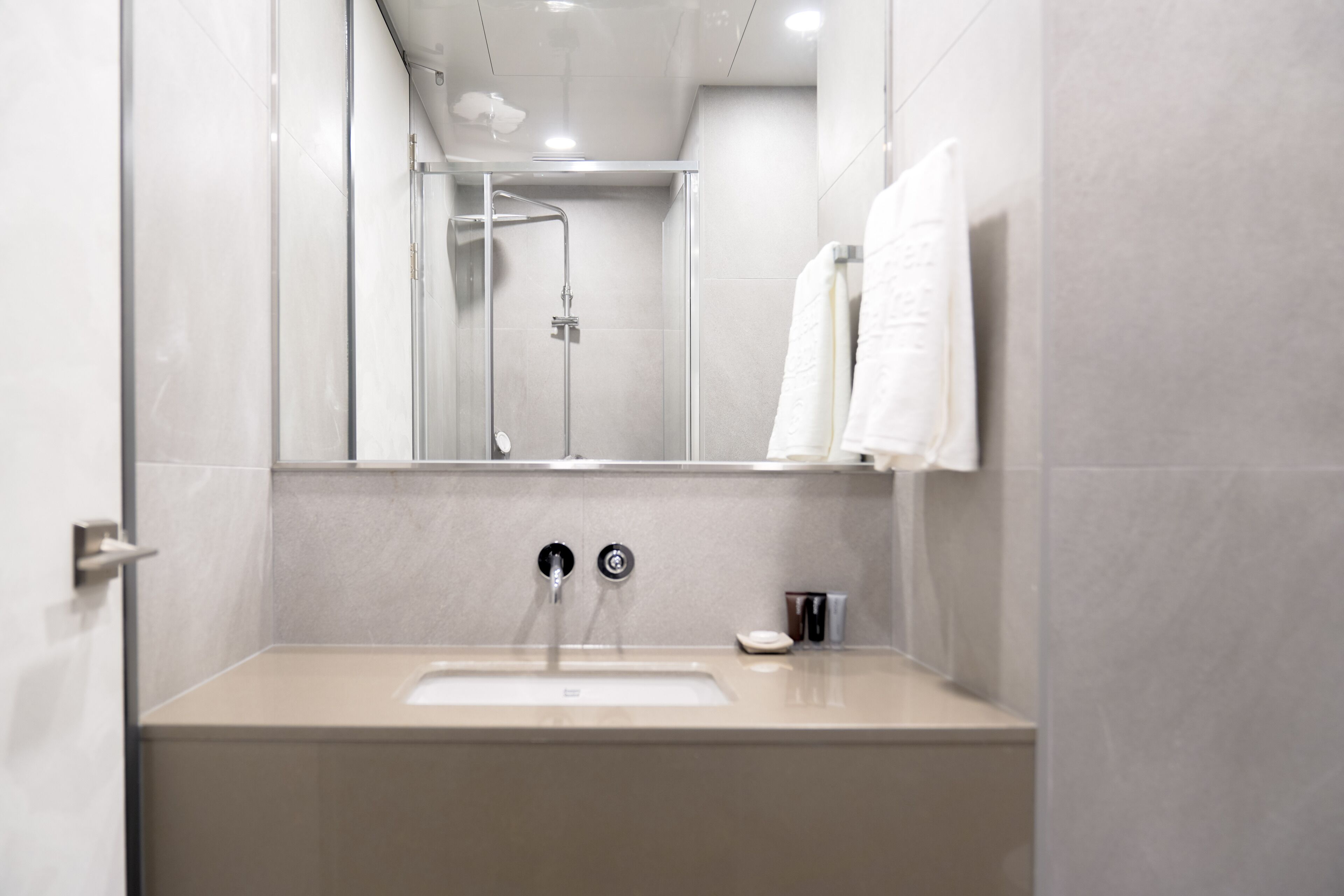 Un baño moderno con ducha de vidrio, un lavamanos beige y un espejo sobre él.