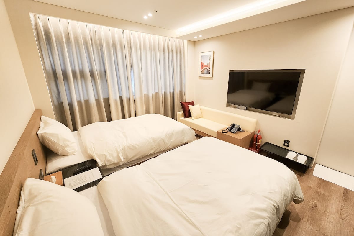 Une chambre d’hôtel avec deux lits, un canapé, une télévision et une fenêtre avec des rideaux.