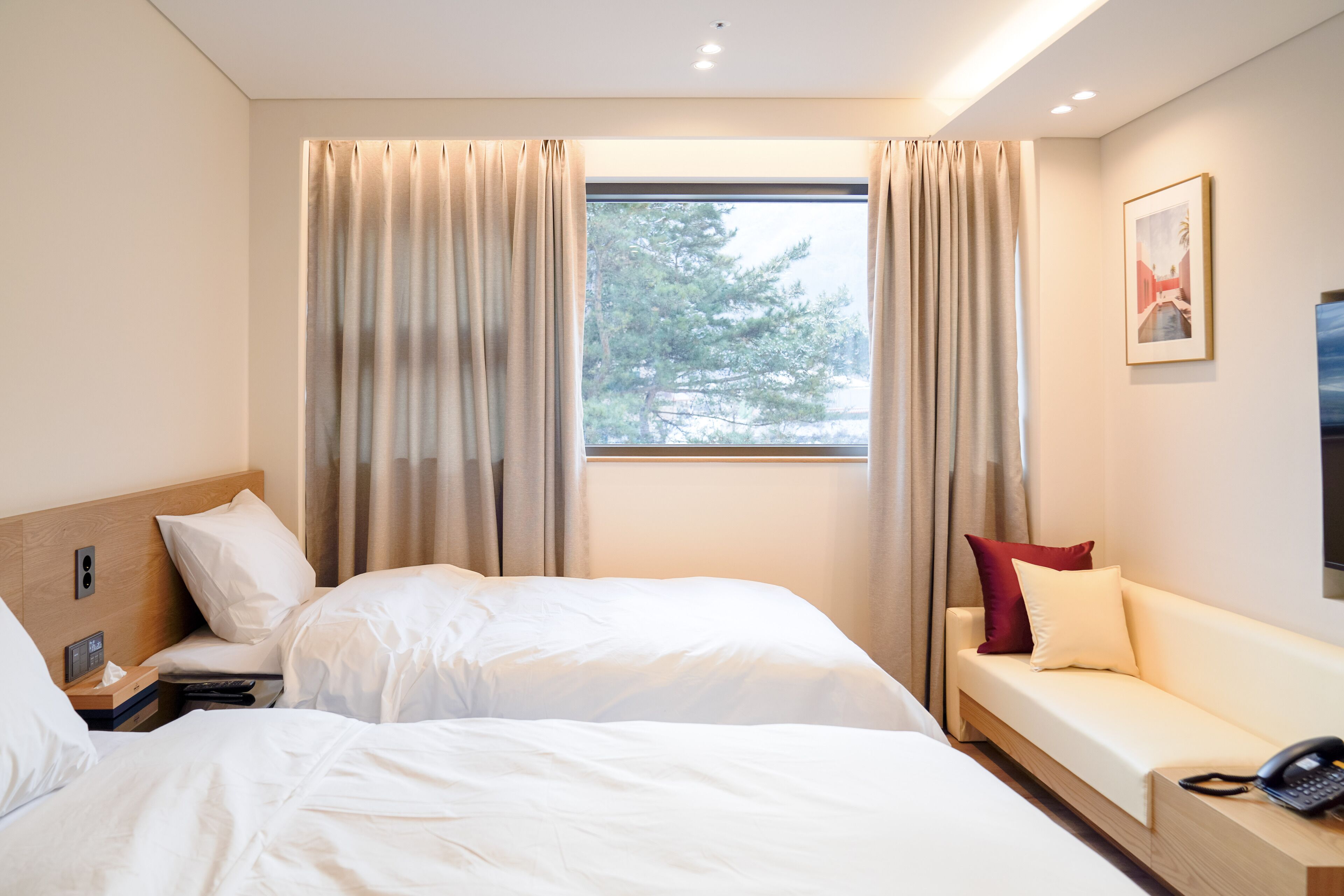 Een hotelkamer met twee bedden, een bank, een raam met gordijnen, een schilderij aan de muur en een telefoon op de bank.