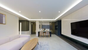 Una sala moderna con sofá, una mesa de centro, un comedor con sillas, un televisor e iluminación empotrada en el techo.