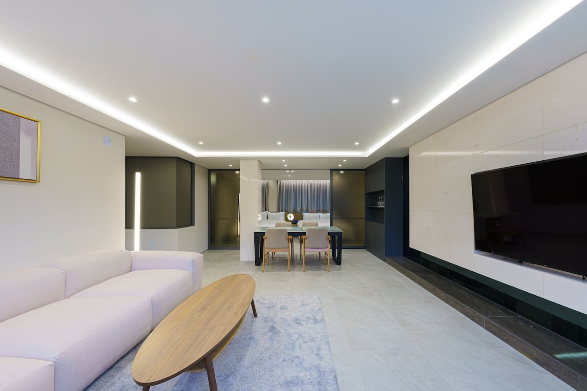 Un salon moderne comprenant un canapé, une table basse, un coin repas avec des chaises, un téléviseur et un éclairage encastré au plafond.