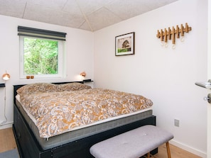 A bedroom with a bed, bench, window, wall-mounted lamp, and a picture.