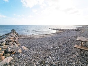 Une plage de galets avec un banc en bois et une digue rocheuse.