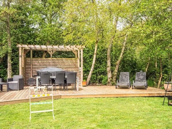 A wooden deck with a pergola, outdoor furniture, and a grill area.