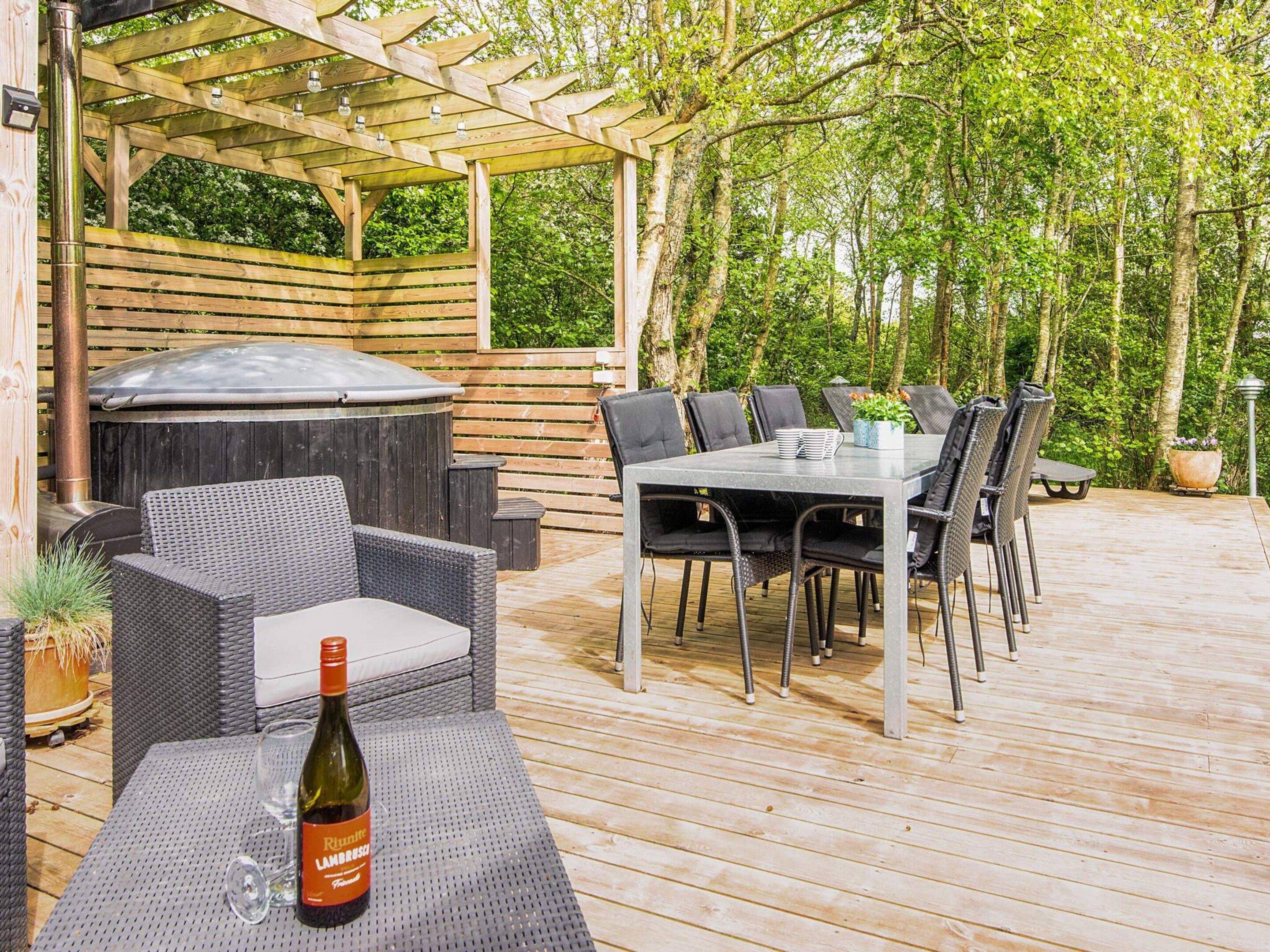 Eine Terrasse im Freien mit Grill, Esstisch, Stühlen und einer Weinflasche.