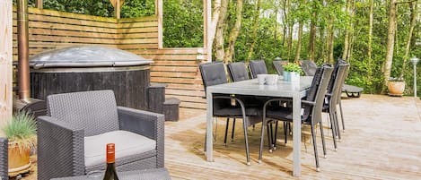 An outdoor patio with a grill, dining table, chairs, and a bottle of wine.