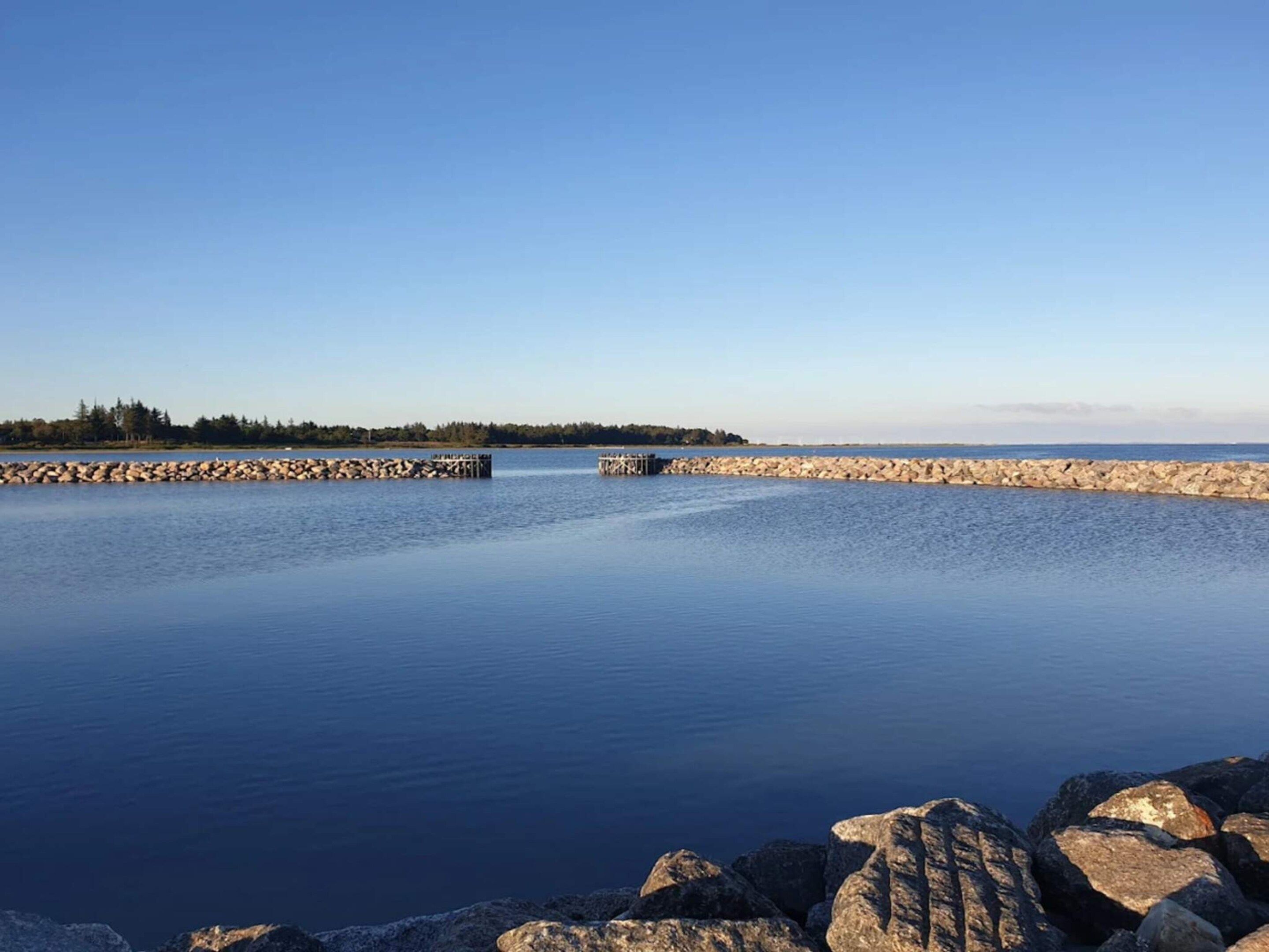 A calm body of water with a rocky shoreline and a clear sky.