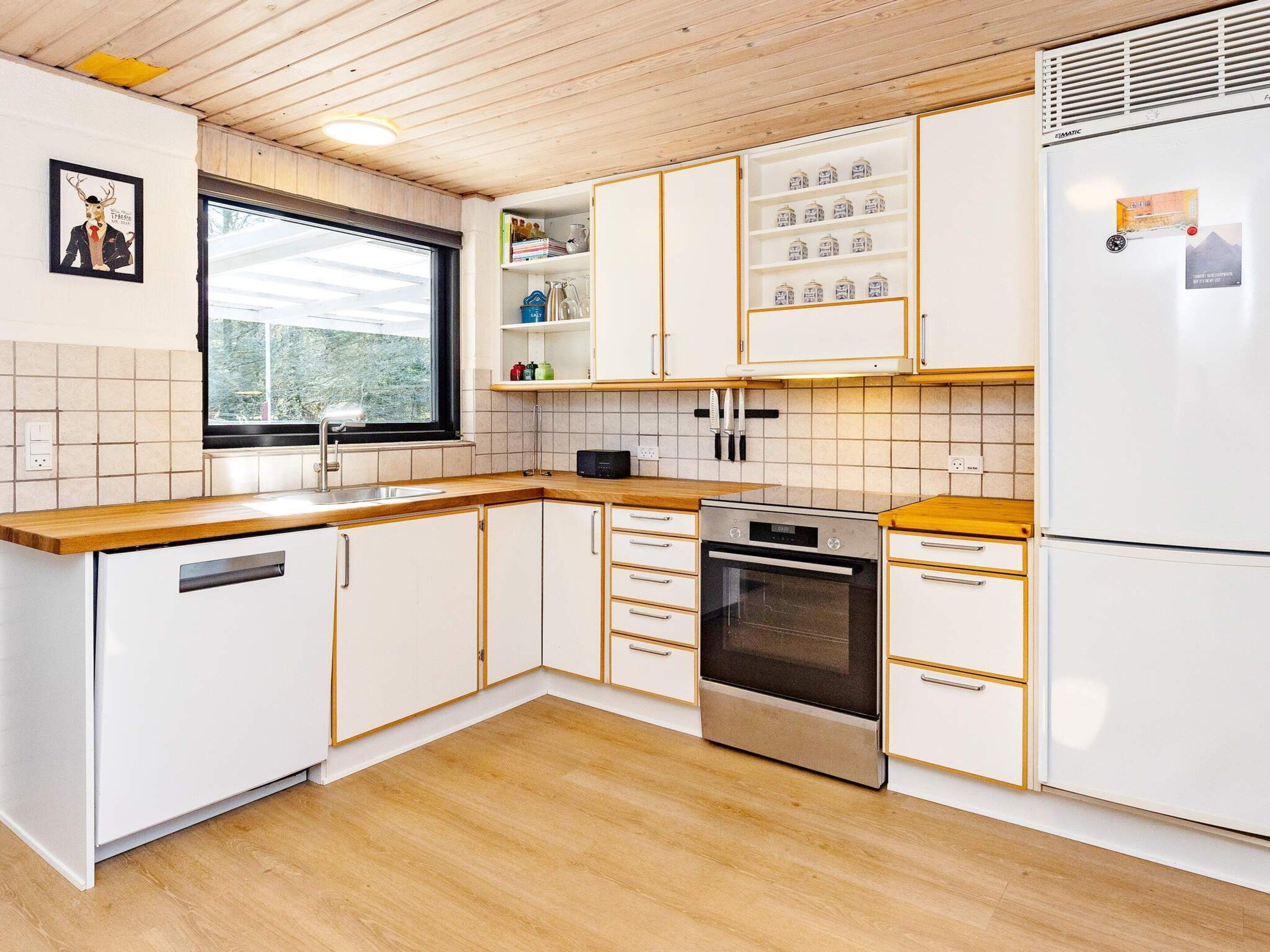 Une cuisine moderne avec des meubles blancs, un four en acier inoxydable et une fenêtre donnant sur les arbres.