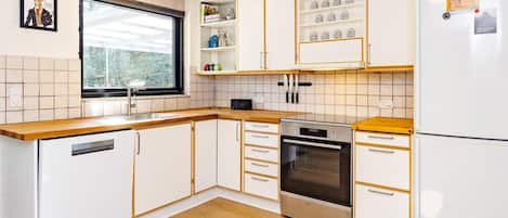 Une cuisine moderne avec des meubles blancs, un four en acier inoxydable et une fenêtre donnant sur les arbres.
