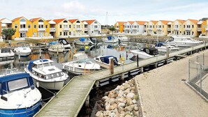 Een jachthaven met aangemeerde boten, een houten looppad en een rij kleurrijke huizen op de achtergrond.