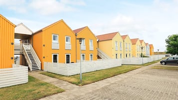 Eine Reihe von gelb-weißen Gebäuden mit Balkonen, ein gepflasterter Gehweg und ein geparktes Auto in der Nähe.
