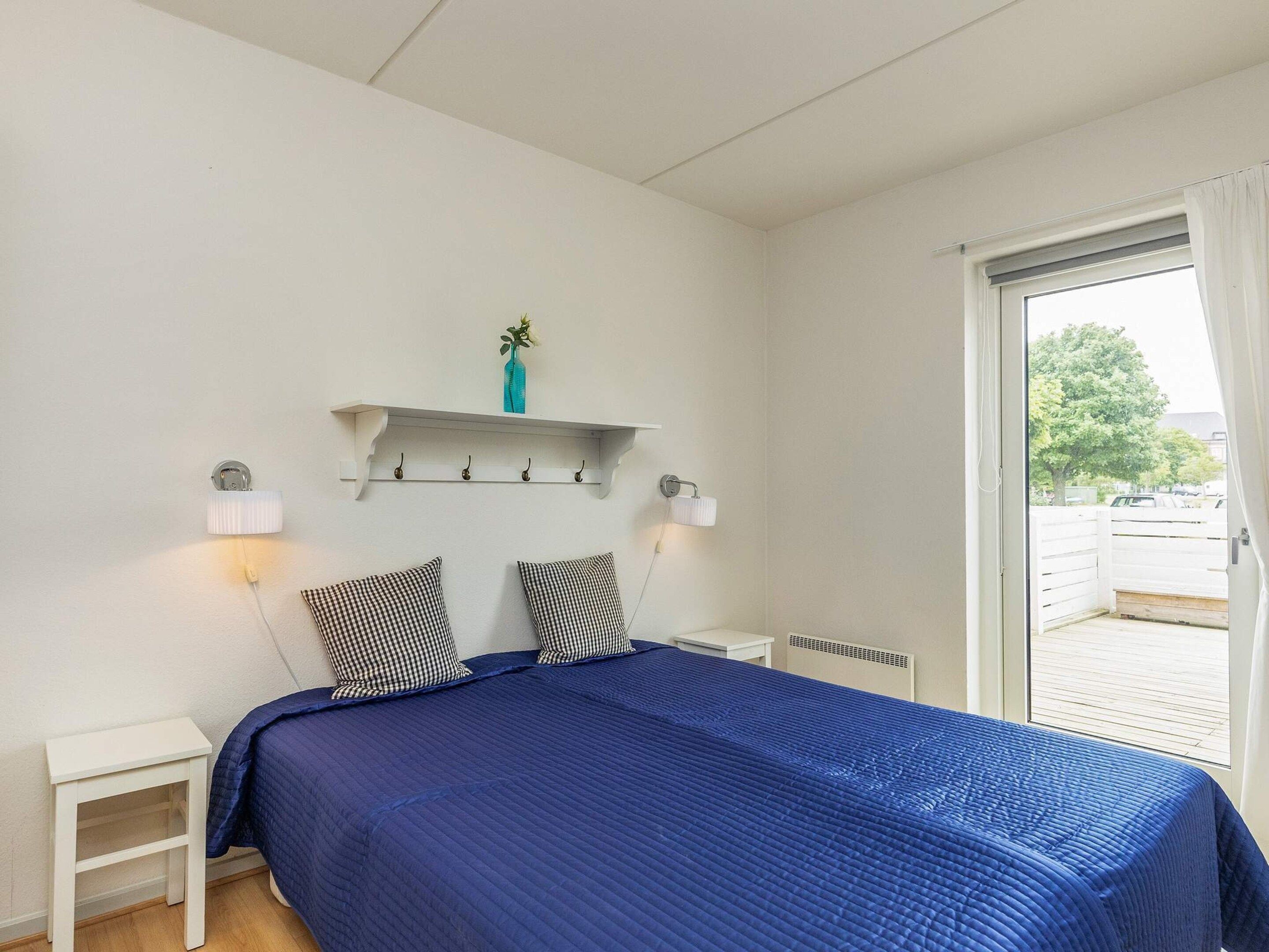 Un dormitorio con cama, mesitas de noche, una estantería con un florero y un ventanal con vistas.