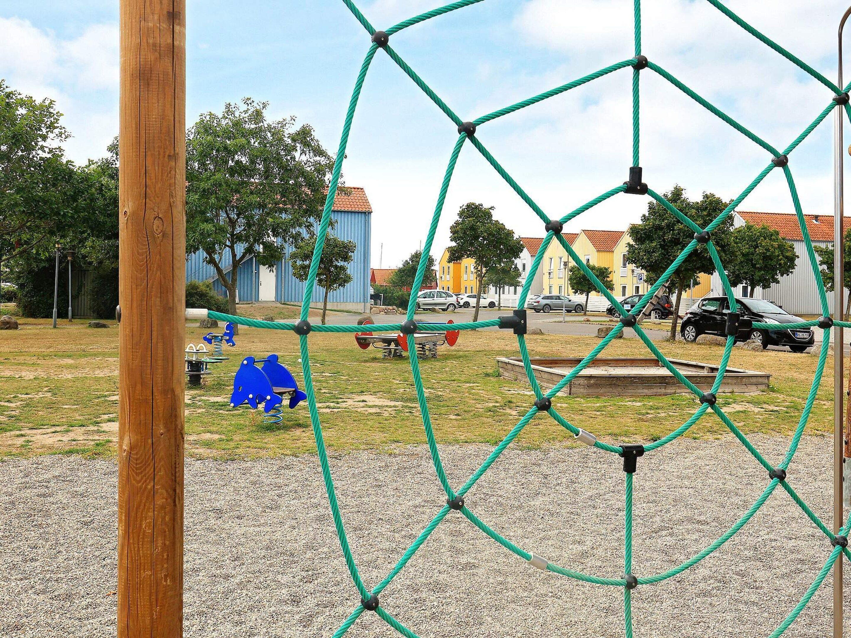 Un’area giochi con una struttura per arrampicata a corda, un palo di legno e una zona con ghiaia.