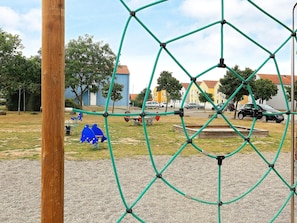 A playground with a rope climbing structure, a wooden post, and a gravel area.