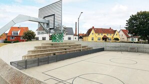 An outdoor basketball court with a metal structure, concrete steps, and a fence.