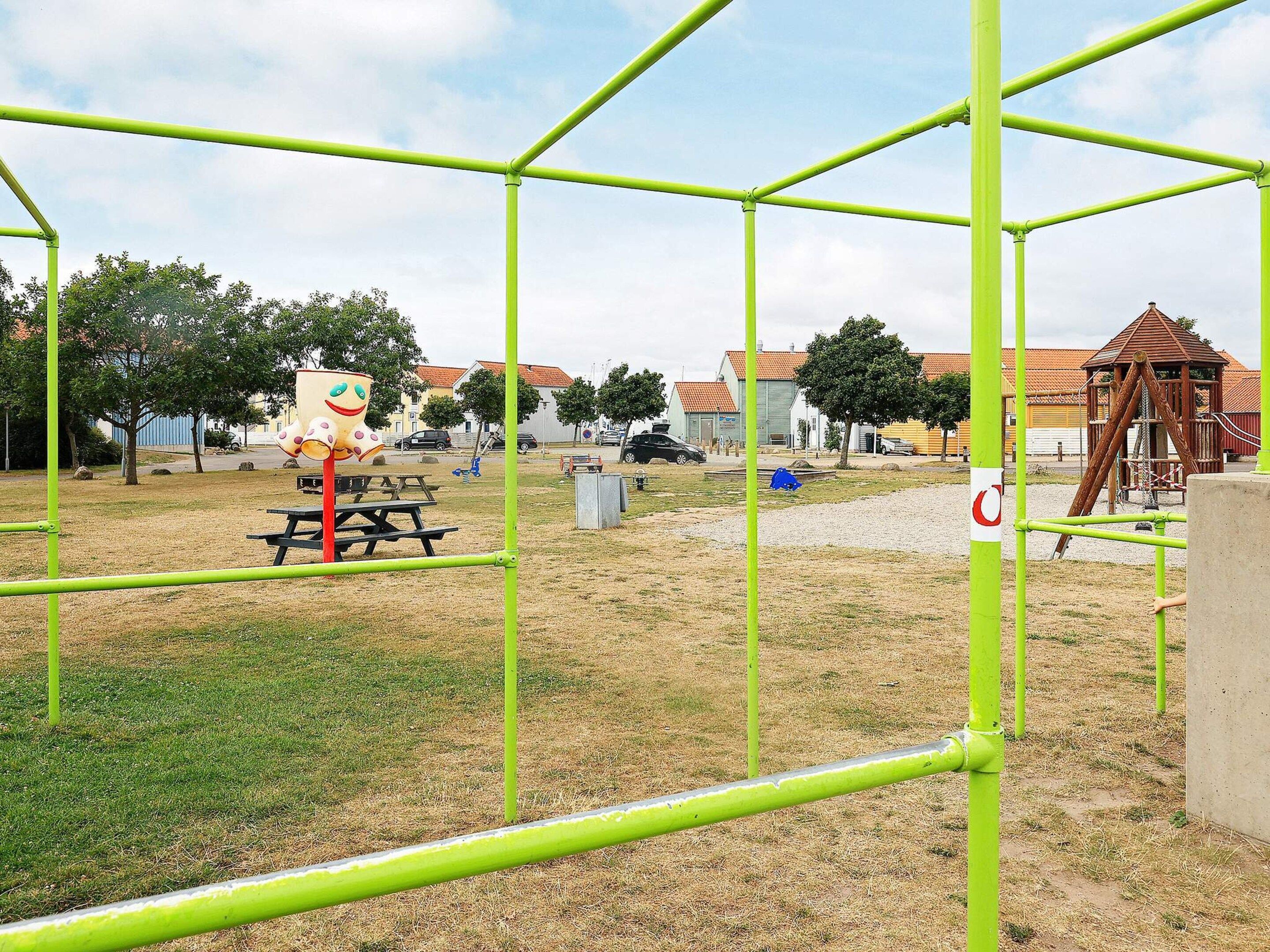 Un parque infantil con estructuras metálicas verdes, una mesa de picnic y un área de juegos.