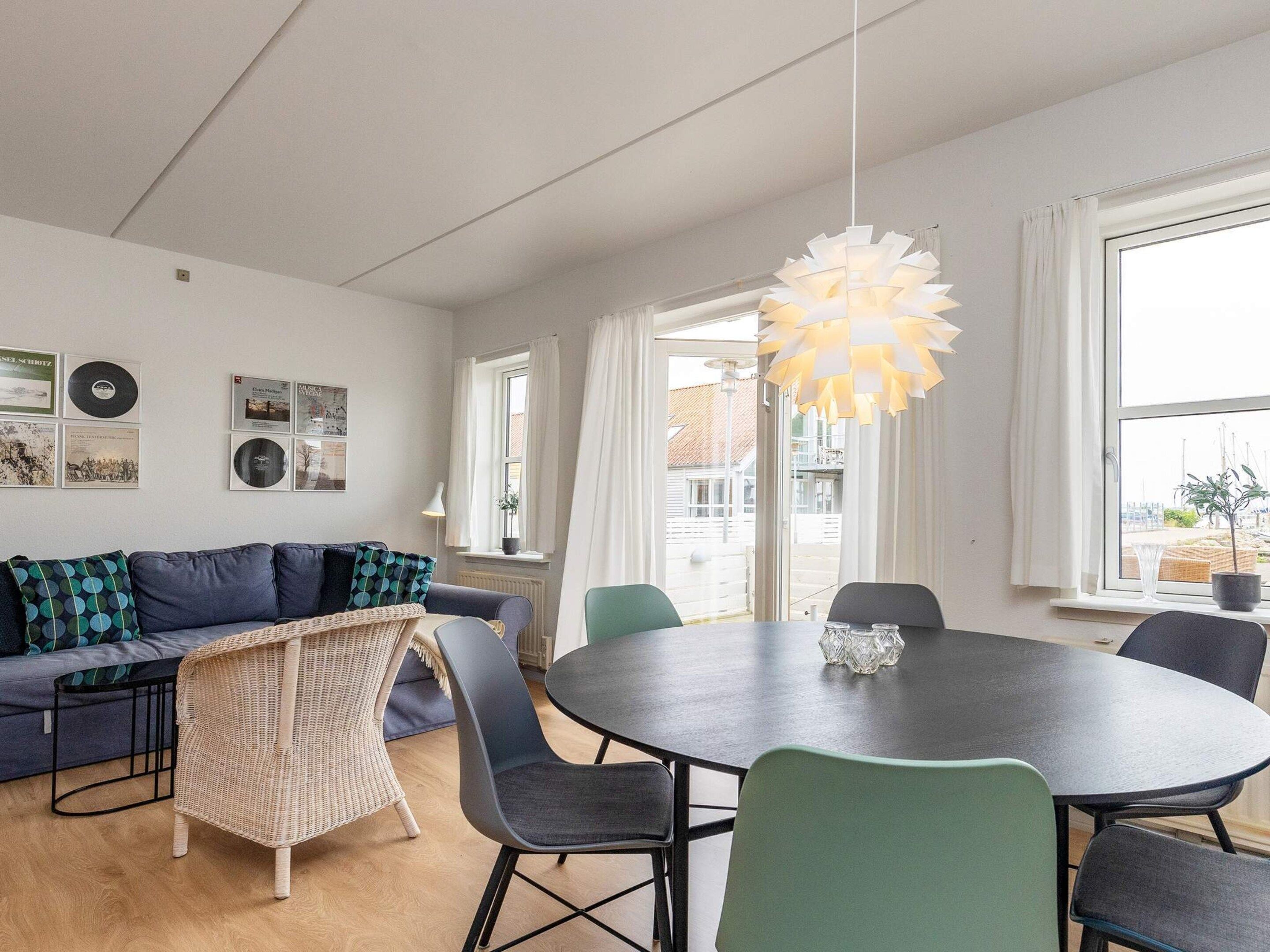 A modern living room with a round dining table, a sofa with patterned cushions, and a hanging light fixture.