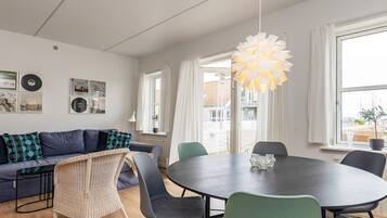 A modern living room with a round dining table, a sofa with patterned cushions, and a hanging light fixture.