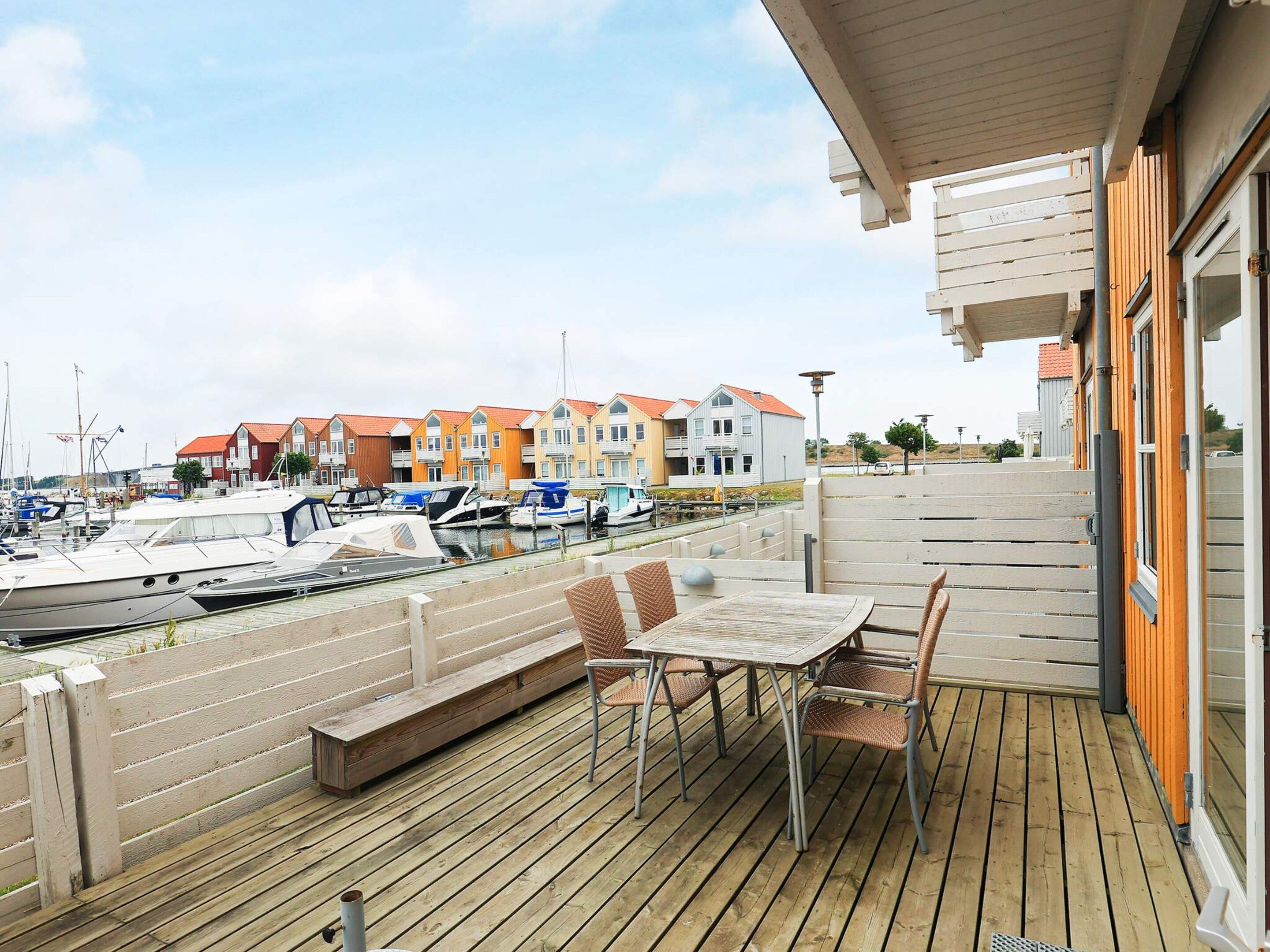 En træterrasse med et bord og stole, med udsigt over en lysthavn med både og farverige bygninger.