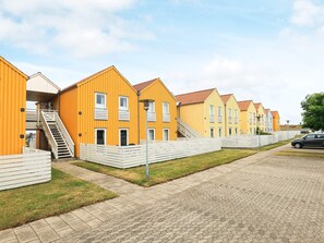 A row of yellow and white buildings with balconies, a paved walkway, and a car parked nearby. - 4 Person Holiday Home in Rudkobing (Rudkobing)