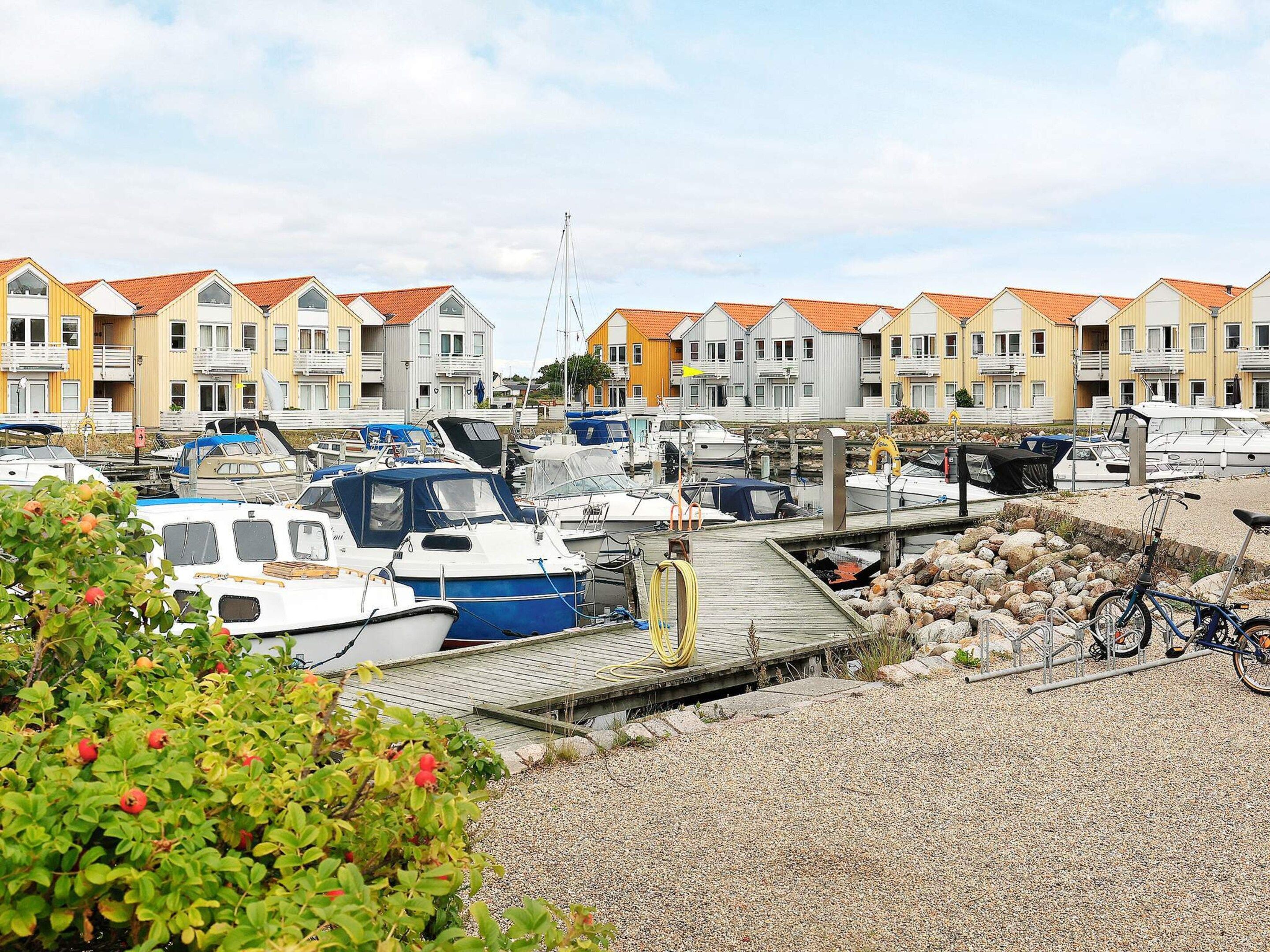 Un puerto deportivo con barcos amarrados, un muelle de madera y casas adosadas al fondo.