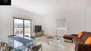 A modern living room with a glass dining table, brown sofa, and a television on a cabinet. - Marina VIEW APT SLPs 9 with private terrace & BBQ (Ta` Xbiex)