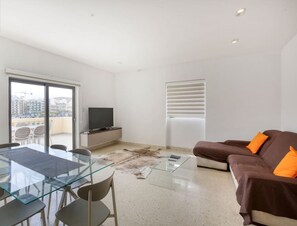 A modern living room with a glass dining table, brown sofa, and a television on a cabinet. - Marina VIEW APT SLPs 9 with private terrace & BBQ (Ta` Xbiex)