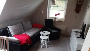 Ett mysigt sovrum på loftvåningen med ett sluttande tak, ett stort fönster med utsikt, ett skrivbord med en dator, en soffa och ett litet bord.